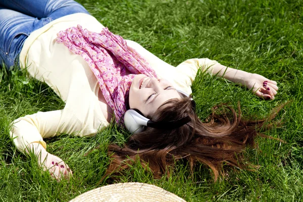 Брюнетка дівчина з навушниками лежить в парку . — стокове фото