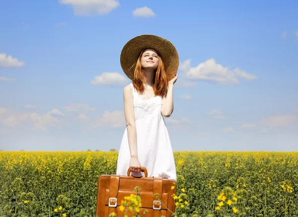Encantadora pelirroja con maleta en campo de colza de primavera . —  Fotos de Stock