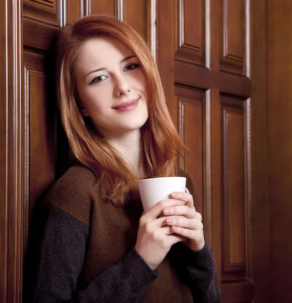 Estilo menina ruiva beber café perto de portas de madeira . — Fotografia de Stock