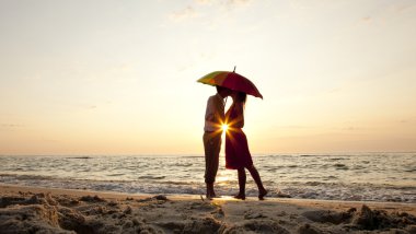 Couple kissing under umbrella at the beach in sunset. clipart
