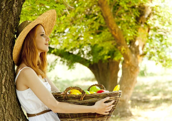 Beautiful redhead girl with fruits in basket at garden. Stock Photo