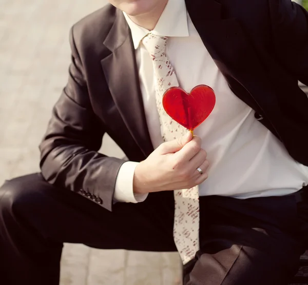 Groom dans une veste de mariage avec un coeur rouge sur sa main — Photo