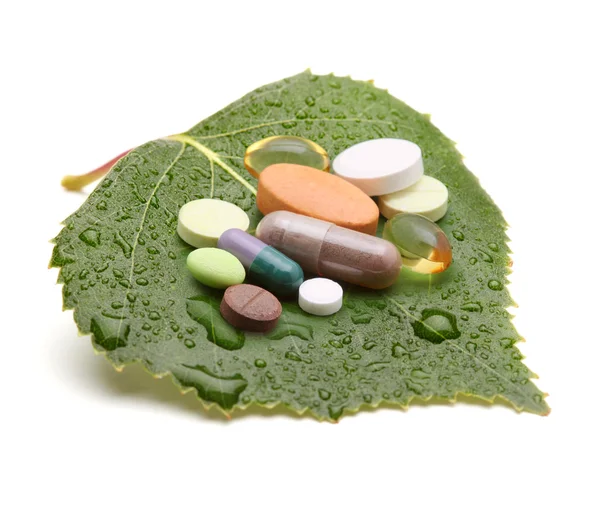 Витамины, таблетки и таблетки на зеленом листе — стоковое фото