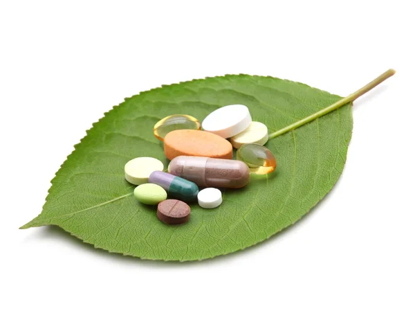 Витамины, таблетки и таблетки на зеленом листе — стоковое фото