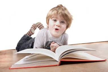 Boy laying on floor pulling a funny face whilst reading book clipart