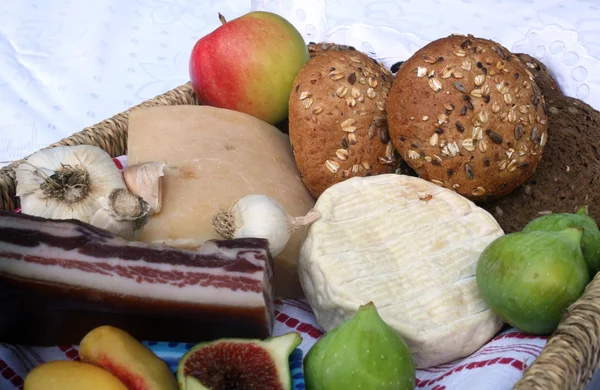 Rústico ainda vida de pão, queijo, bacon e figos em uma cesta de vime — Fotografia de Stock