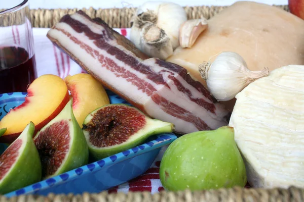 Rustik stilleben av ost, bacon och frukter i en flätad korg — Stockfoto