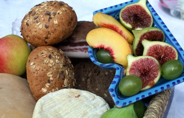 Natura morta rustica di pane, formaggio, pancetta e frutta in un cesto di vimini — Foto Stock