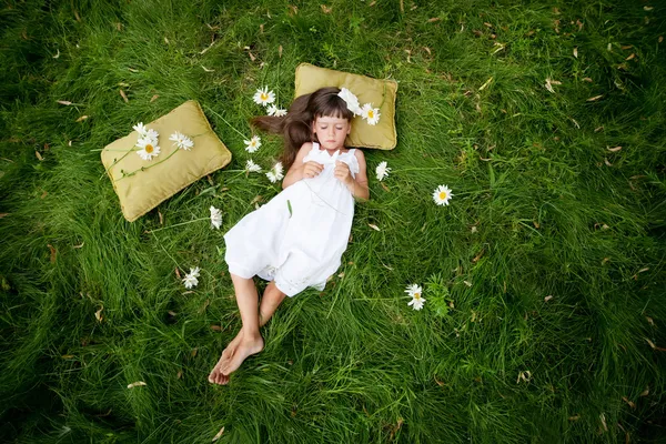 어린 소녀가 싱싱 한 봄 풀에서 부드러운 베개 위에서 쉬고 있다 — 스톡 사진