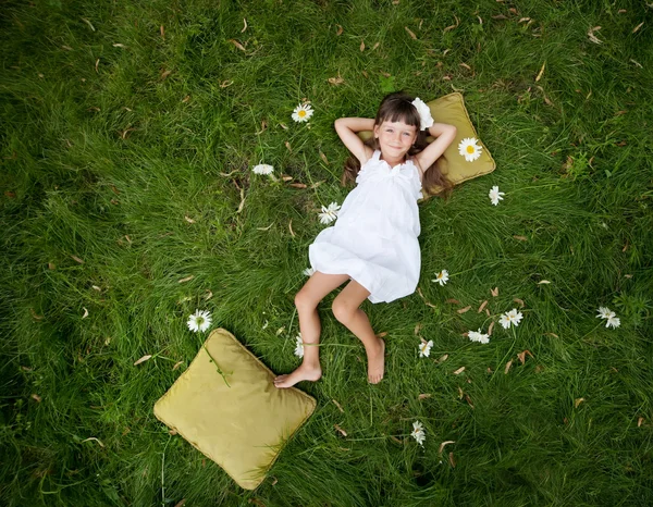 Liten flicka vilar på mjuk kudde i färsk vår gräs — Stockfoto