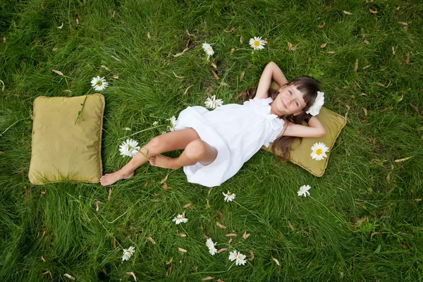 Kleines Mädchen ruht auf weichen Kissen im frischen Frühlingsgras — Stockfoto