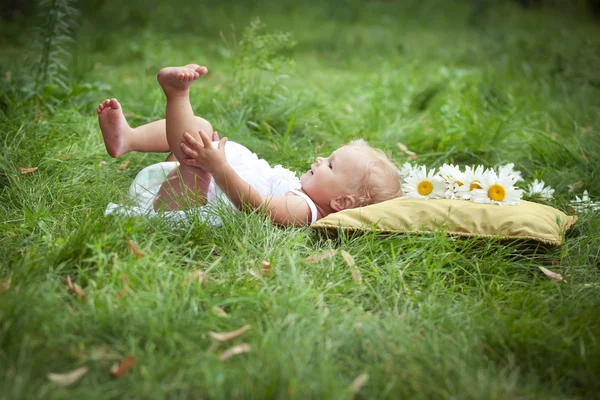 Little girl on soft pillow in fresh spring grass — Stock Photo, Image