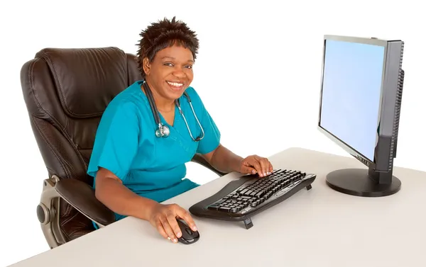 Enfermeira afro-americana sorrindo para a câmera enquanto sentada na mesa — Fotografia de Stock