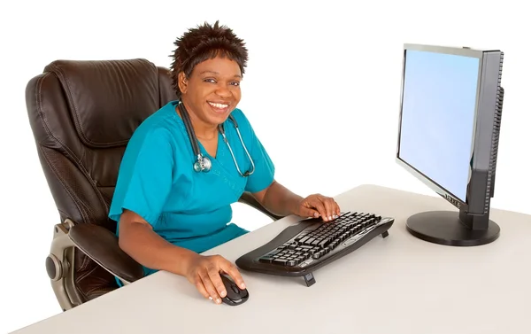 坐在桌前的同时在相机微笑的非洲裔美国护士 免版税图库图片