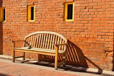 Wooden Bench Sitting by Orange Brick Wall with Yellow Windows clipart