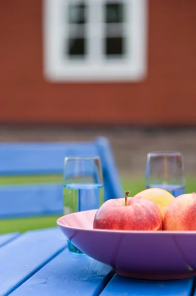 Maçãs e copos com água em uma mesa de jardim — Fotografia de Stock