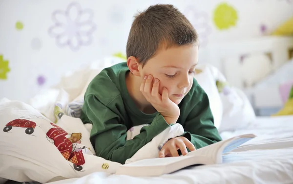 Pojke läser en bok i sängen — Stockfoto