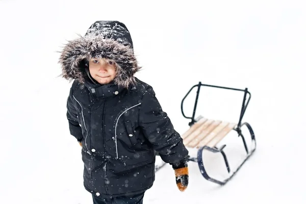 Jonge jongen in winter pak trekken sleeën — Stockfoto