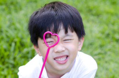 Cute Asian boy holding a heart shape on his eye clipart