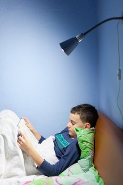 Kid reading a book at bedtime clipart