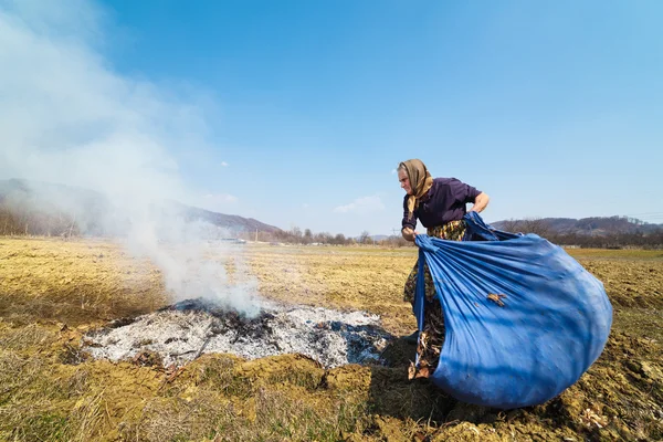 Старшая сельская женщина сжигает опавшие листья — стоковое фото