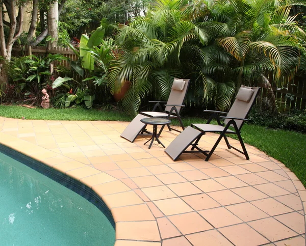 Dos sillas reclinables junto a una piscina rodeada de jardín tropical —  Fotos de Stock
