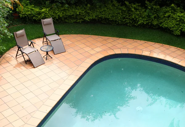 Duas cadeiras reclináveis ao lado de uma piscina rodeada por jardim tropical — Fotografia de Stock