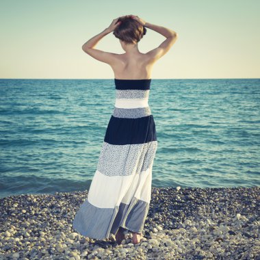 Güzel genç bir kadın sahilde duruyor.