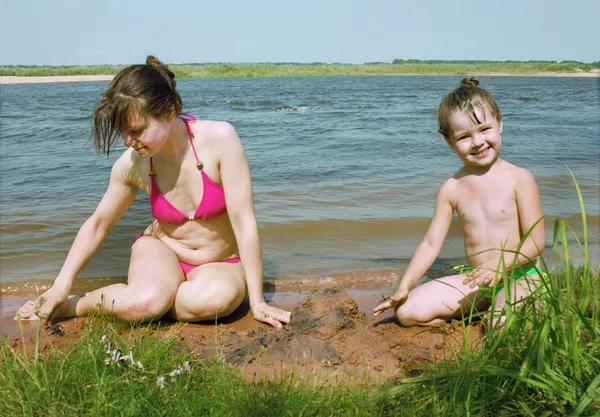 Mamá con una hija jugar en la orilla del río — Foto de Stock