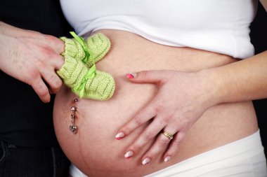 Dad holding gree knit bootees on pregnant belly clipart