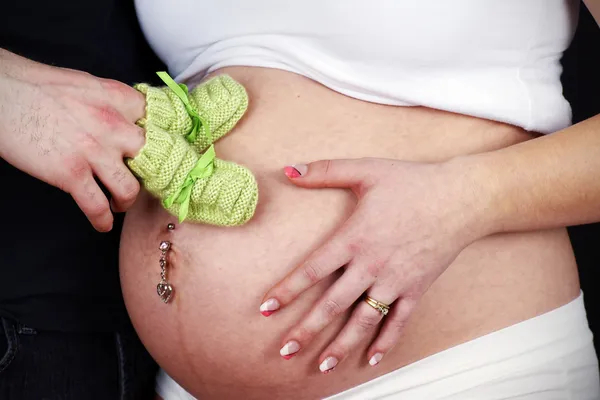 Papa houden gree brei bootees op zwangere buik — Stockfoto