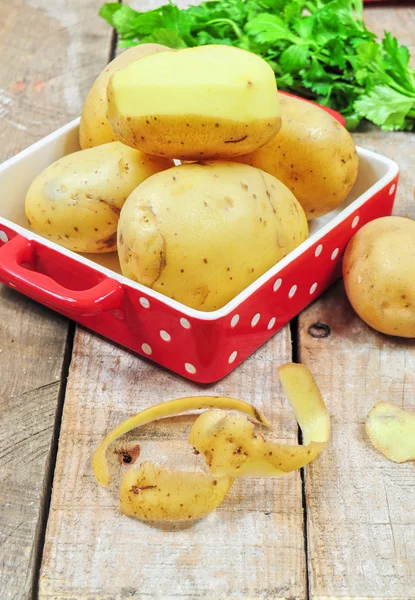 Raw potatoes in red tray and potato peels — Stock Photo, Image