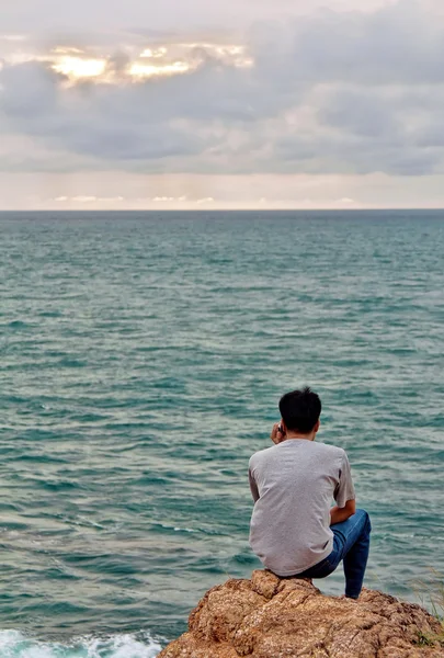 一名男子看上去入海坐在石头上 — 图库照片
