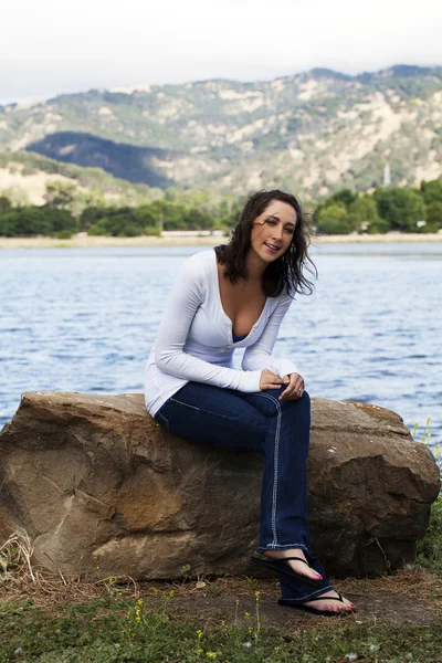 Junge kaukasische Frau sitzt auf Felsen am Seeufer — Stockfoto