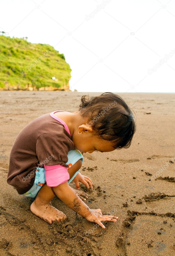 Asian toddler girl writing on beach sand