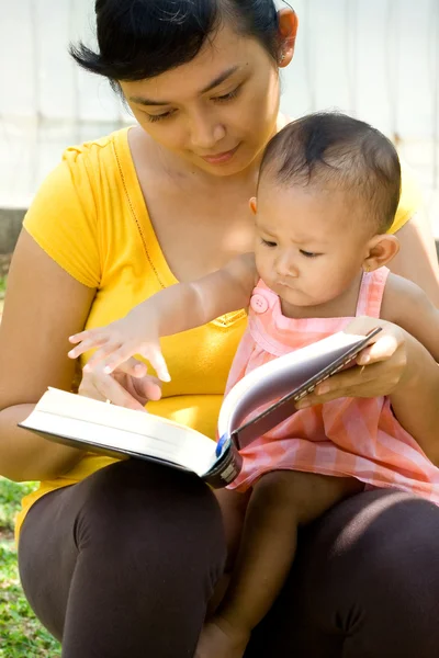 Etnische jonge moeder lezen terwijl babysit kind — Stockfoto