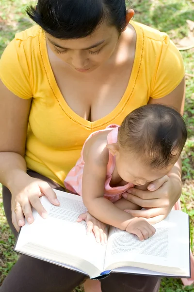 Mãe étnica lendo enquanto babá — Fotografia de Stock