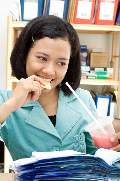 Νεαρή γυναίκα τρώγοντας και πίνοντας στην εργασία — Φωτογραφία Αρχείου