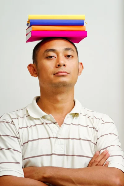Zelfverzekerde Aziatische jonge man met boeken op hoofd — Stockfoto