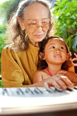 Ethnic child and grandmother playing piano clipart