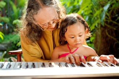 Asian senior woman and child playing piano clipart