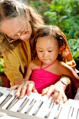 Ethnic elderly woman teach child play piano clipart