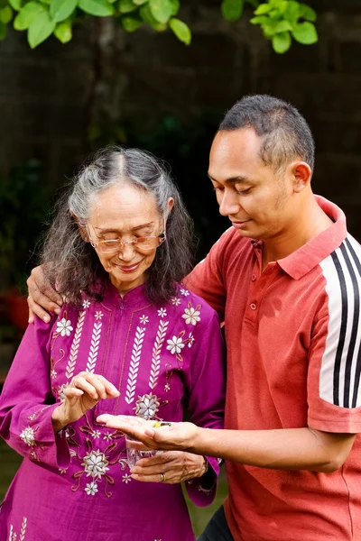 Азіатських молода людина обійми і допомогти старенькою матір'ю, приймаючи ліки — стокове фото