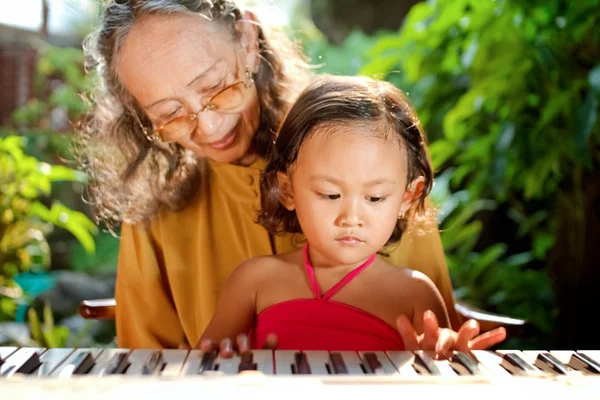 Etnické dětí a babička hrát na klavír — Stock fotografie