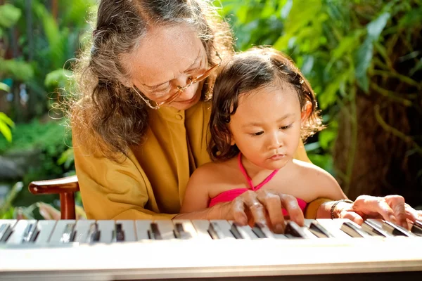 Азиатская старшая женщина и ребенок играют на пианино — стоковое фото