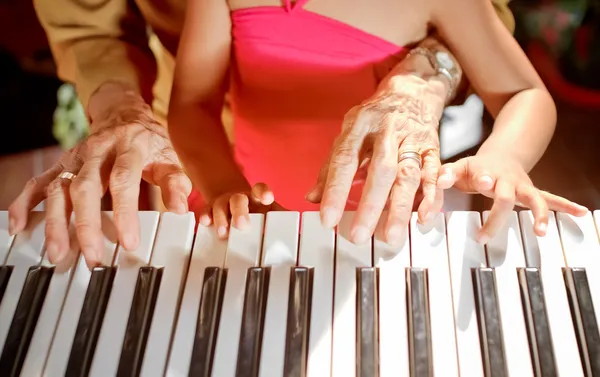 Руки пожилой женщины и ребенка, играющие на пианино — стоковое фото