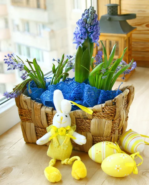Flores de primavera en una pequeña cesta y Pascua de conejo — Foto de Stock