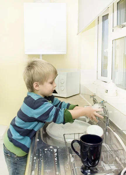 Little boy in the kitchen washing taps.