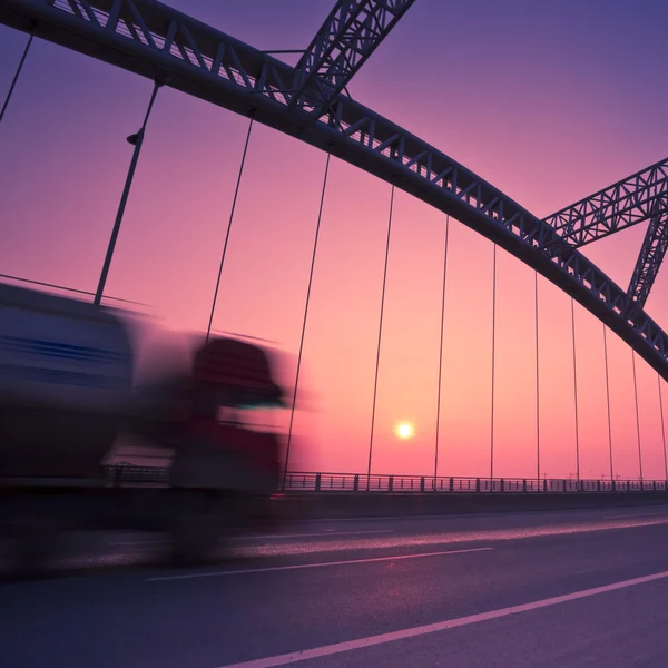 LKW rast bei Sonnenuntergang durch eine Brücke, Bewegungsunschärfe. — Stockfoto