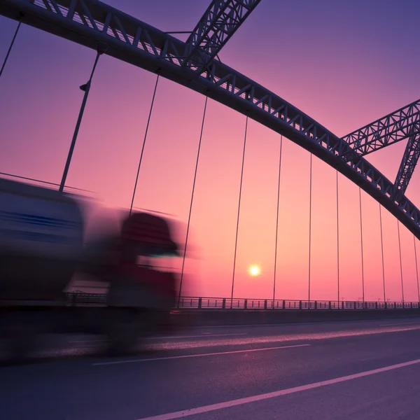 Caminhão acelerando através de uma ponte ao pôr do sol, borrão de movimento . — Fotografia de Stock